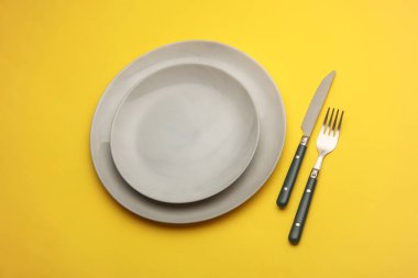 Sarı arka planda çatal bıçak takımı olan tabaklar. Masa ayarı. Üst görünüm