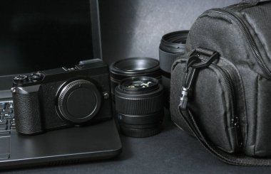 Profesyonel fotoğrafçı ekipmanı. Laptop, fotoğraf çantası, kamera ve siyah arka planda lens.