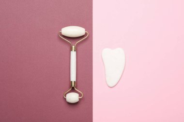 Masaj silindiri ve gua sha kazıyıcı. Pembe bordo arka planda yaşlanma karşıtı yüz masajı için.