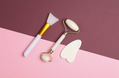 Masaj silindiri ve yaşlanma önleyici yüz masajı için gua sha kazıyıcı, pembe bordo arka planda vücut yağı spatulası. Üst görünüm