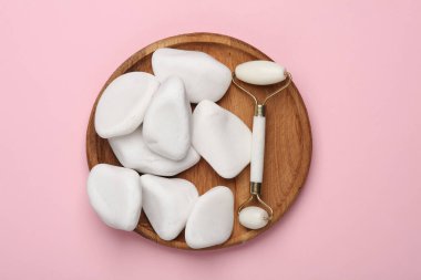 Yaşlanma önleyici yüz masajı için masaj makinesi, pembe arka planda çakıl taşı.