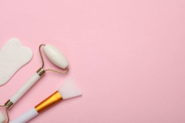 Yeşim yüz silindiri ve gua sha kazıyıcı, pembe arka planda vücut yağı spatulası. Üst görünüm