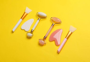 Yeşim yüz silindirleri ve sarı arka planda gua sha kazıyıcıları. Güzellik konsepti