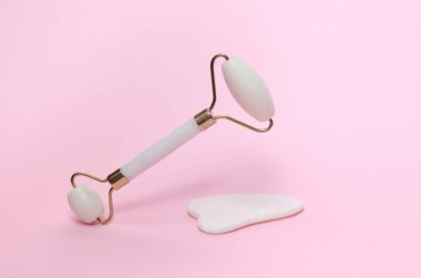Yeşim yüz silindiri ve pembe arka planda gua sha kazıyıcı. Güzellik konsepti.
