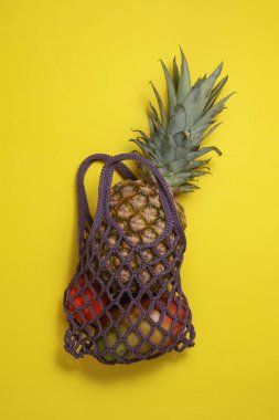 Sarı arka planda ananas ve tropikal meyvelerle dolu bir ip torbası.