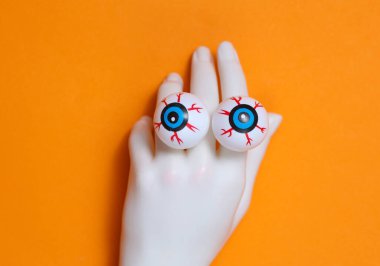 Turuncu arka planda gözleri olan plastik el. Cadılar Bayramı hayat dolu