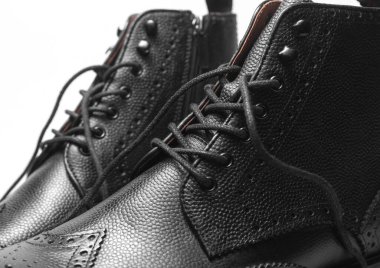 Beyaz arka planda bağcıkları çözülmüş siyah deri erkek çizmeleri.