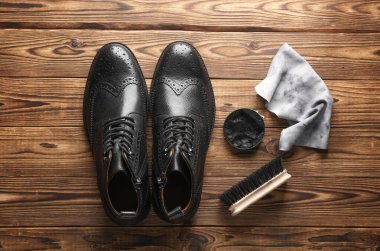 Ahşap zemin üzerinde ayakkabı cilası, paçavra ve fırça olan siyah çizmeler. Deri ayakkabılar