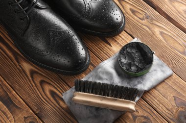 Ahşap zemin üzerinde ayakkabı cilası, paçavra ve fırça olan siyah çizmeler. Deri ayakkabılar