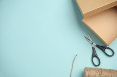 DIY, Ürün ambalajlama, sunum. Mavi zemin üzerinde makas ve iplik içeren Kraft karton kutu.