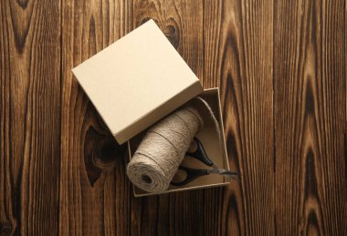 DIY, Ürün ambalajlama, sunum. Tahta zemin üzerinde makas ve iplik içeren Kraft karton kutu.
