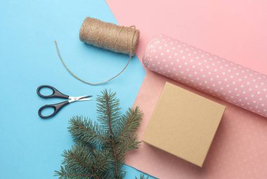 El işi kutusu, iplik ve makas karışımlı ambalaj kağıdı mavi-pembe pastel arka planda. Üst Manzara. Düz yatıyordu