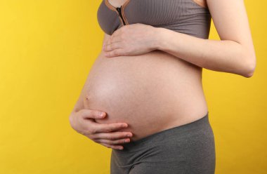 Sarı arka planda karnını tutan hamile bir kadın.