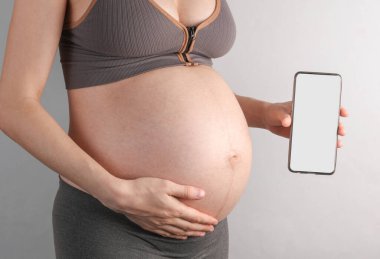 Hamile kadın elinde gri arka planda beyaz ekranlı bir akıllı telefon tutuyor. Tasarım için model