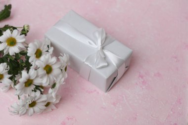 Beyaz hediye kutusu ve pembe beton arka planda bir buket çiçek.