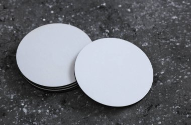 Beyaz yuvarlak boş bardak altlıkları. Koyu beton arka planda bir model.