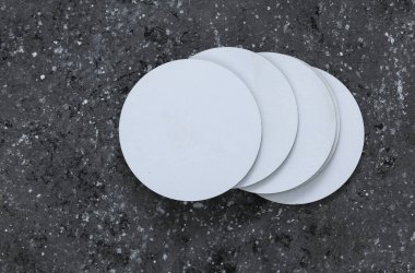 Beyaz yuvarlak boş bardak altlıkları. Koyu beton arka planda bir model.