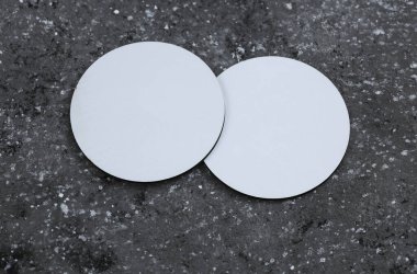 Beyaz yuvarlak boş bardak altlıkları. Koyu beton arka planda bir model.