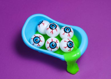 Cadılar Bayramı, mor arka planda balçık ve göz küreleriyle dolu oyuncak banyosuyla dolu.