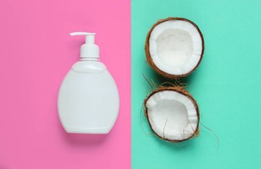 Hindistan cevizi şampuanı. Şampuan şişesi, mavi-pembe pastel arka planda hindistan cevizi yarıları. Minimalist güzellik düzlüğü