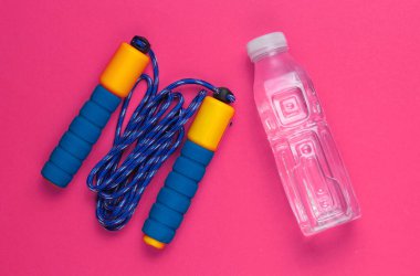 Düz yatış tarzı spor konsepti. İp atlama, bir şişe su. Pembe arka planda spor malzemeleri. Üst görünüm