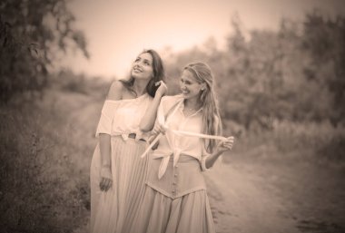 Eski moda giysiler içinde iki neşeli duygusal en iyi kız arkadaş yaz bulutlu bir günde iniş boyunca yürürler. Birlikte yürüyün.