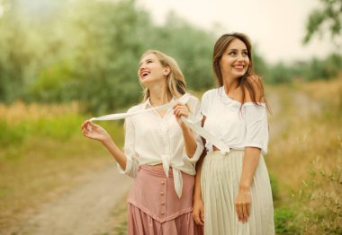 Eski moda giysiler içinde iki neşeli duygusal en iyi kız arkadaş yaz bulutlu bir günde iniş boyunca yürürler. Birlikte yürüyün.