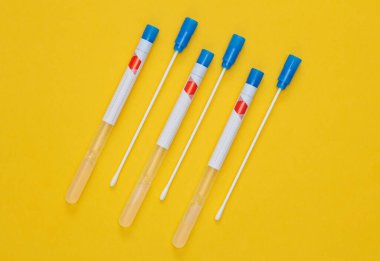 Çubukta çubuk olan tıbbi test tüpleri, sarı arka plan.