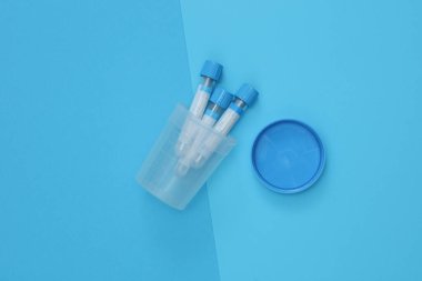 Tıbbi kan testi tüpleri ve idrar testi kavanozu mavi arka planda.