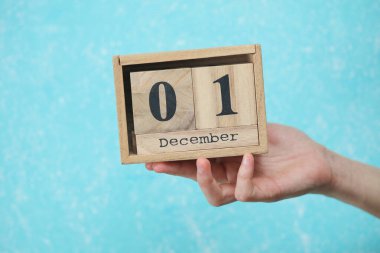 Kadının elinde ahşap blok takvimi var. Tarihi Aralık 01, mavi beton arka plan.