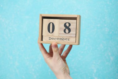 Kadının elinde ahşap bloklama takvimi var. Üzerinde de mavi beton arka plan tarihi var.