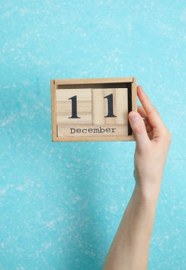 11 Aralık tarihli ahşap bloklama takvimi mavi beton arka planda kadının elinde.