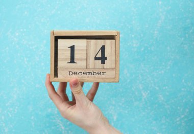 Kadının elinde ahşap blok takvimi var. Tarihi 14 Aralık, mavi beton arka plan.