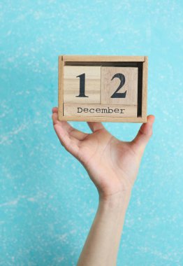 Kadının elinde ahşap blok takvimi 12 Aralık tarihli mavi beton arka planda