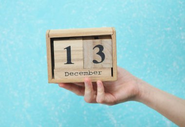 Kadının elinde ahşap blok takvimi var. Tarihi 13 Aralık, mavi beton arka plan.
