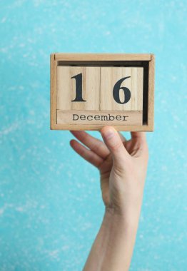 Kadının elinde ahşap blok takvimi var. Tarihi 16 Aralık, mavi beton arka plan.