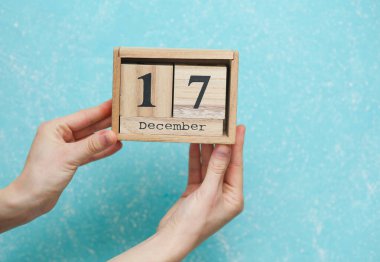 Kadının elinde ahşap blok takvimi var. 17 Aralık 'ta mavi beton arka planda.