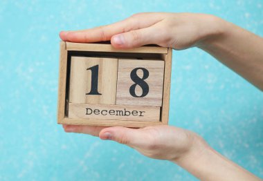 Kadının elinde ahşap blok takvimi var. Tarihi 18 Aralık, mavi beton arka plan.