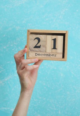 Kadının elinde ahşap blok takvimi var. Tarihi 21 Aralık, mavi beton arka plan.