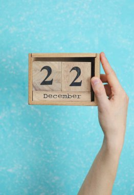 22 Aralık tarihli ahşap blok takvimi mavi beton arka planda kadının elinde.