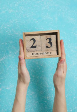 23 Aralık tarihli ahşap bloklama takvimi mavi beton arka planda kadının elinde.