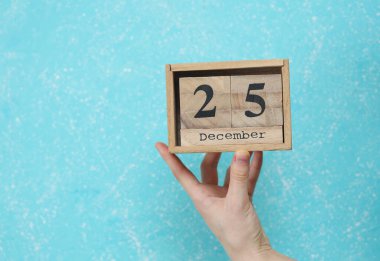 25 Aralık tarihli ahşap blok takvimi mavi beton arka planda kadının elinde.