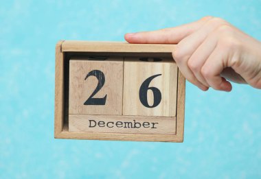 26 Aralık tarihli ahşap blok takvimi mavi beton arka planda kadının elinde.