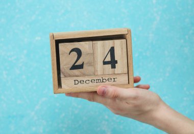 24 Aralık tarihli ahşap blok takvimi mavi beton arka planda kadının elinde.