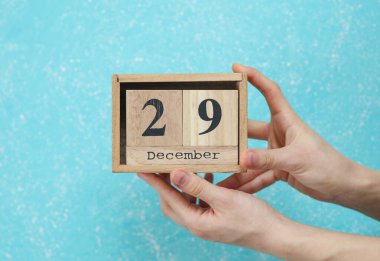 29 Aralık tarihli ahşap blok takvimi mavi beton arka planda kadının elinde.