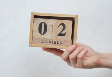 Kadının elinde tahta blok takvimi var. Tarihi Ocak 02, beyaz beton arka plan.