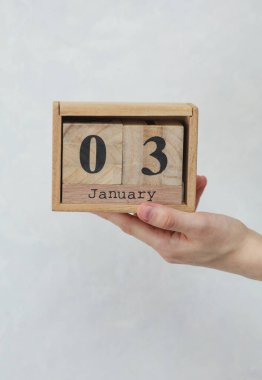 Kadının elinde tahta blok takvimi var. Tarihi Ocak 03, beyaz beton zemin üzerinde.