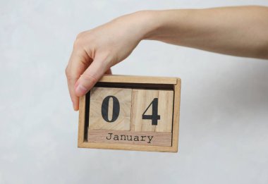 Kadının elinde tahta blok takvimi var. Beyaz beton arka planda Ocak 04 tarihli.