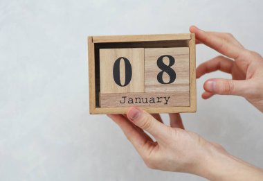 Kadının elinde tahta bloklama takvimi var. Tarihi, 8 Ocak, beyaz beton arka planda.