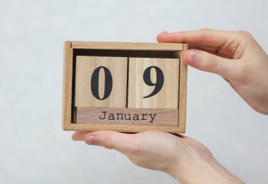 Kadının elinde tahta blok takvimi var. Tarihi 09 Ocak, beyaz beton arka planda.